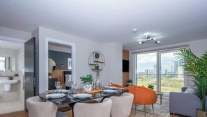 A modern dining area with a table set for four, a sofa, and a large window offering a city view. - Luxury Waterfront 2BR - Free Gym Access & Parking (Stretford)