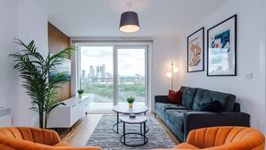 A modern living room with a sofa, two armchairs, a small table, and a large window offering a city view. - Waterfront 2BR | 2 Bath | Free Gym + Parking (Manchester)
