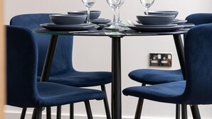 Een eetgedeelte met een tafel voor drie personen, blauwe stoelen en een ingelijst kunstwerk aan de muur.