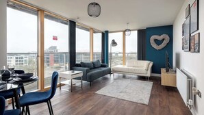 Een moderne woonkamer met een bank, een eettafel en stoelen. Een groot raam biedt uitzicht op gebouwen.