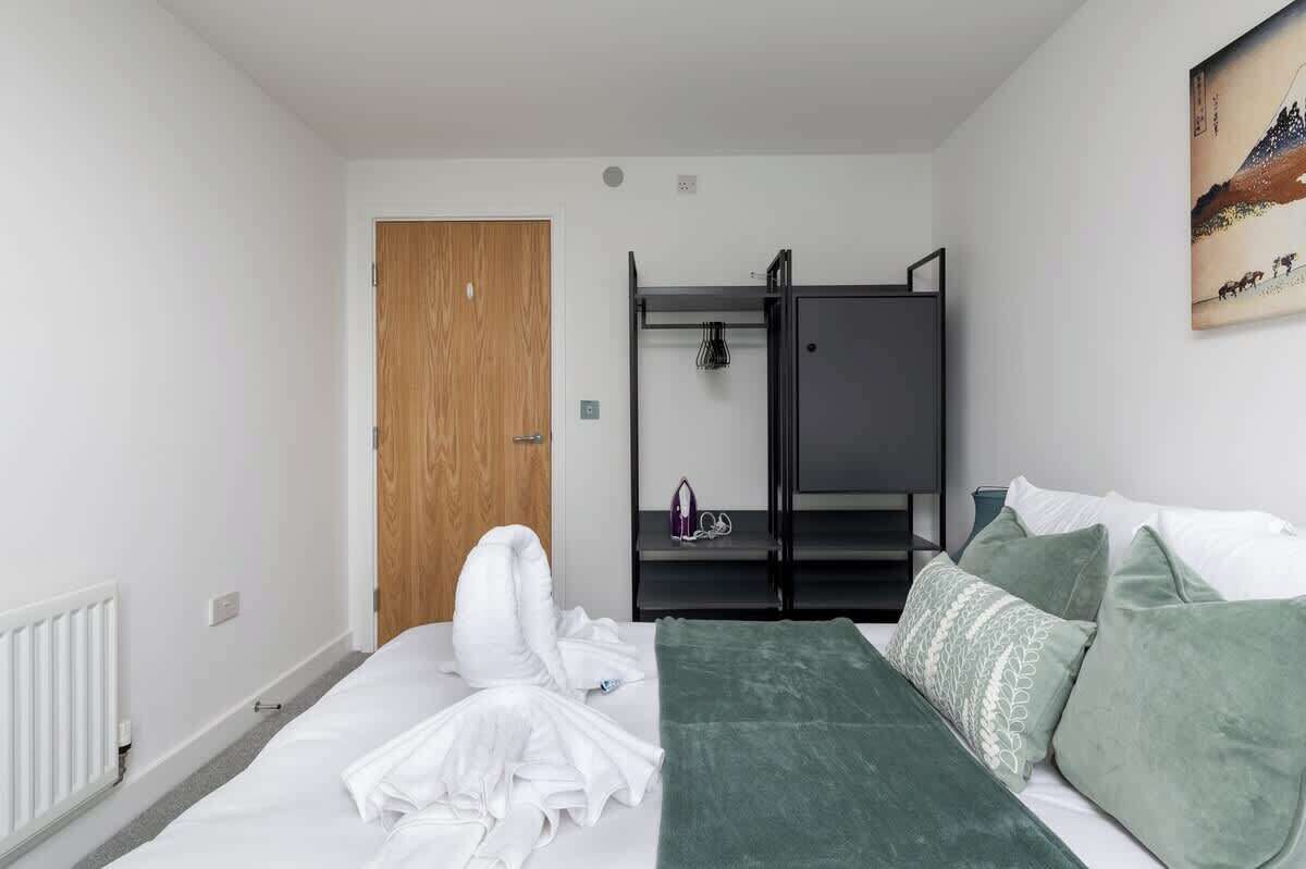 A bedroom with a bed, a wooden door, a black wardrobe, and a painting on the wall.