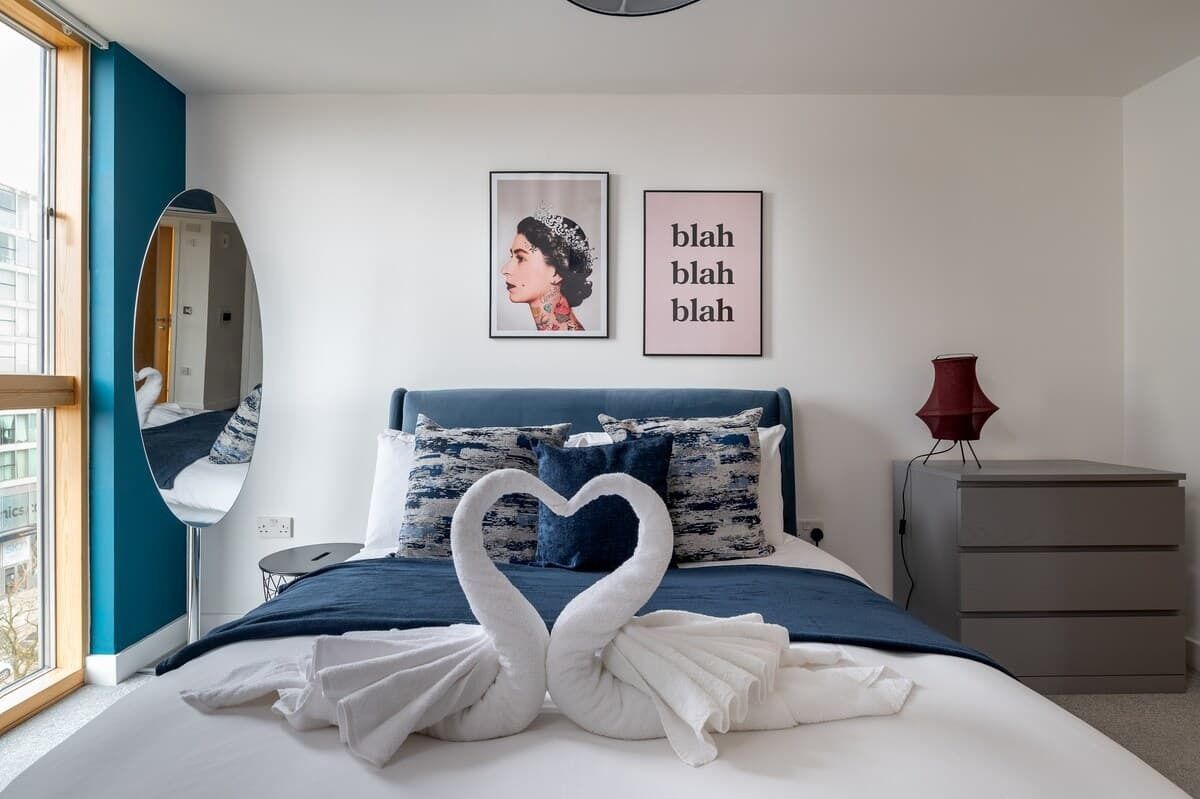 A bedroom with a bed, a mirror, a dresser, and wall art.