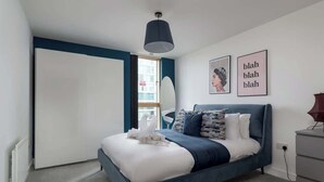 Een moderne slaapkamer met een bed, nachtkastje, lamp en raam.