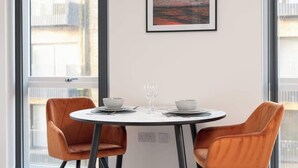 A dining area with a round table, two chairs, and a framed picture of a sunset. - Luxury 1Bed| Canal Views|Free Parking|Central MK (Milton Keynes)