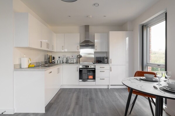 A modern kitchen with white cabinets, stainless steel appliances, and a marble countertop.