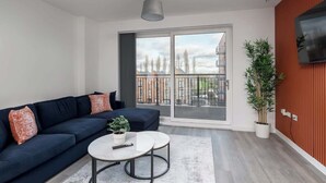 A modern living room with a dark blue sofa, a round coffee table, and a large sliding glass door leading to a balcony. - Luxury 1Bed| Canal Views|Free Parking|Central MK (Milton Keynes)