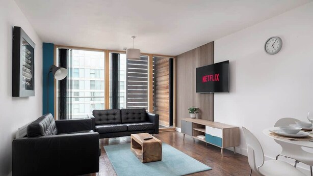 Un soggiorno moderno con un divano nero, un tavolino in legno e una TV che mostra il logo di Netflix.
