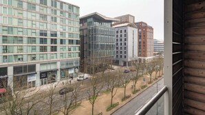 Una vista di una strada urbana moderna con edifici, tra cui una struttura a più piani con facciata in vetro e un edificio più piccolo con facciata rossa.