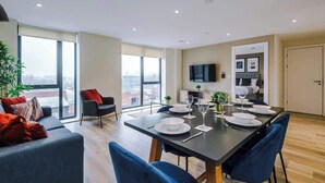 A modern living room with a dining area, large windows, a flat-screen TV, and a city view.