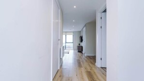 A modern hallway with wooden flooring, white walls, and a door at the end.
