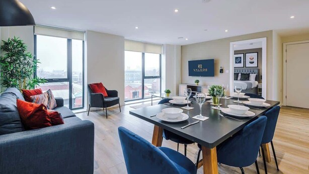 A modern living room with a dining area, large windows, a flat-screen TV, and a city view.