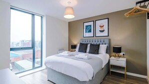 A modern hotel room with a large bed, a bedside table, a nightstand, and a view of the city through a large window.