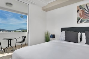 Une chambre dâhĂŽtel avec un lit, un petit balcon dotĂ© dâune table et de chaises, une lampe et un tableau au mur.
