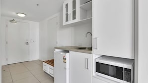 A compact kitchen with white cabinets, a microwave, a sink, and a small refrigerator. - Coastal Chic in Heart of Cairns with Rooftop Pool (Cairns)