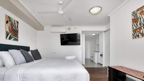 A modern hotel room with a bed, a ceiling fan, a flat-screen TV, and artwork on the walls. - Coastal Chic in Heart of Cairns with Rooftop Pool (Cairns)