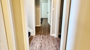 Un couloir doté d’un plancher en bois et de murs blancs, qui mène à une porte au fond.