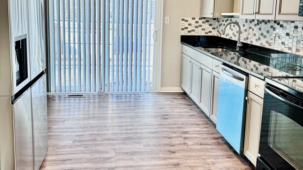 Une cuisine moderne avec un plancher en bois, des appareils électroménagers en acier inoxydable et un dosseret carrelé.
