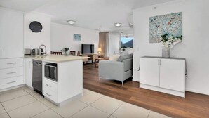Una cocina moderna con muebles blancos, una zona de comedor con un sofá gris y una sala de estar con un sofá gris y un cuadro.