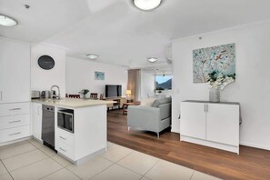 A modern kitchen with white cabinetry, a dining area with a grey sofa, and a living room with a grey sofa and a painting.