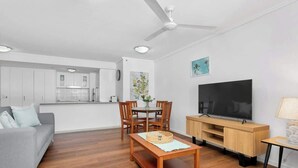 Una sala de estar moderna con sofá, mesa de comedor, televisor y área de cocina.