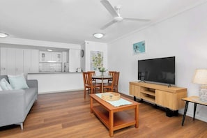 A modern living room with a sofa, dining table, TV, and kitchen area.