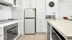 Una cocina moderna con armarios blancos, un refrigerador de acero inoxidable, un horno empotrado y una encimera grande.