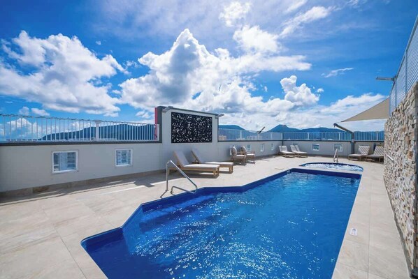 Una piscina en la azotea con sillas de descanso, un biombo decorativo y vistas despejadas a las montañas.