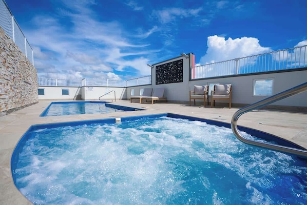 Un espace piscine sur le toit, comprenant deux bains à remous, des chaises longues et un ciel dégagé.