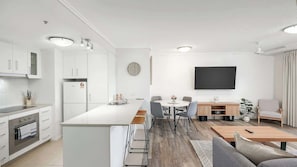 Una cucina moderna con mobili bianchi, un'isola centrale e un'area da pranzo con sedie e tavolo.