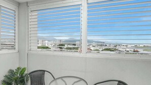 A balcony with a view of a cityscape, a potted plant, and two wicker chairs. - Seaside Azul—A Central Studio with Rooftop Pool (Cairns)