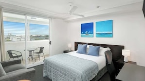 A hotel room with a bed, a desk, a chair, a balcony with chairs, and artwork on the wall. - Seaside Azul—A Central Studio with Rooftop Pool (Cairns)