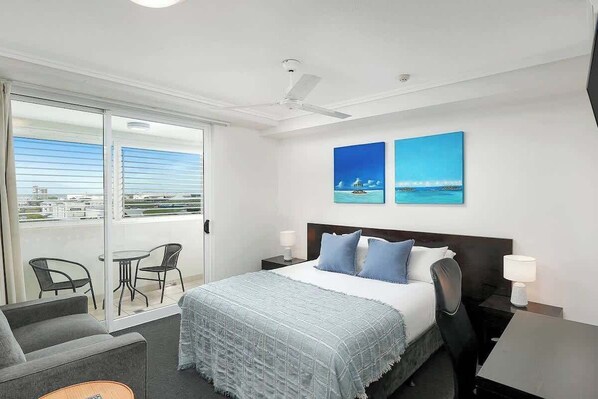 A hotel room with a bed, a desk, a chair, a balcony with chairs, and artwork on the wall. - Seaside Azul—A Central Studio with Rooftop Pool (Cairns)