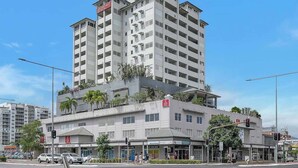 A multi-story hotel with balconies, a central plaza, and various shops at street level. - Seaside Azul—A Central Studio with Rooftop Pool (Cairns)