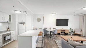 Una cucina moderna con mobili bianchi, un'isola centrale e un'area da pranzo con sedie e tavolo.