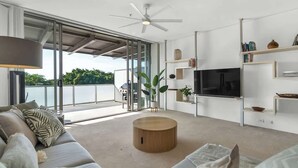 A modern living room with a large TV, a ceiling fan, and a view of the outdoors.