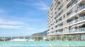 A hotel with a pool, a view of the sea, and a mountainous backdrop.