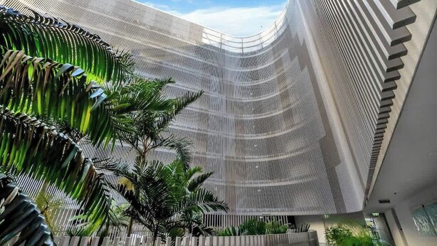 A modern building with a curved facade, a series of vertical lines, and a palm tree in the foreground.