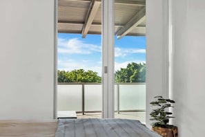 Una stanza con un letto, una pianta in vaso e vista su un balcone con una porta vetrata.