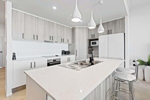 Una cucina moderna con mobili bianchi, un'isola centrale, elettrodomestici in acciaio inossidabile e luci a sospensione.