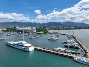 Un porto turistico con numerosi yacht ormeggiati, una grande nave da crociera e vista su montagne in lontananza.