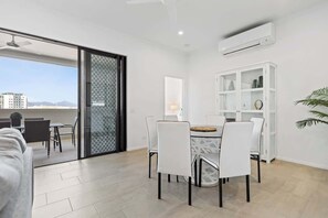 Un salon moderne comprenant un coin repas, une porte-fenêtre coulissante donnant sur un balcon, une bibliothèque blanche et un ventilateur de plafond.