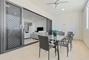 Un espace repas moderne avec une table et des chaises en verre, un ventilateur de plafond et une porte-fenêtre coulissante donnant sur la cuisine.