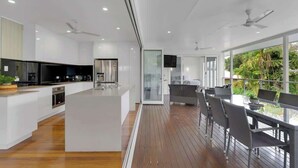 A modern kitchen with a central island, a dining area with outdoor seating, and a large sliding glass door leading to a balcony.