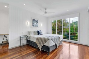 Una camera da letto con un letto, una scrivania, una lampada da terra, una ventola a soffitto e un'ampia finestra vista sul verde.