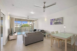 Un soggiorno moderno con divano, tavolo da pranzo e sedie, una ventola a soffitto e un'ampia finestra con vista.