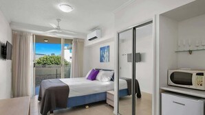 A bedroom with a bed, a nightstand, a microwave, and a sliding glass door to a balcony. - Resort-Style Cityview Getaway in Perfect Location (Cairns)