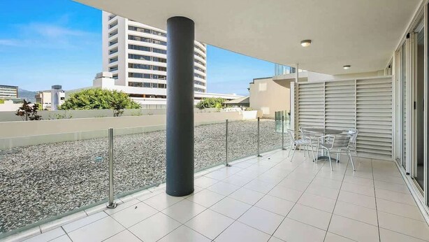 A balcony with a tiled floor, a metal railing, and a glass door leading to an indoor area. - Resort-Style Cityview Getaway in Perfect Location (Cairns)