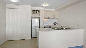 A compact kitchen with white cabinets, a built-in sink, and a refrigerator. - Resort-Style Cityview Getaway in Perfect Location (Cairns)
