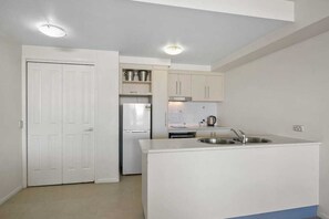 Una cocina compacta con armarios blancos, un lavamanos integrado y un refrigerador.