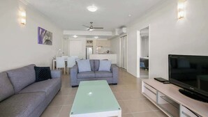 A modern living room with a sofa, a coffee table, a TV, and a ceiling fan. - Resort-Style Cityview Getaway in Perfect Location (Cairns)
